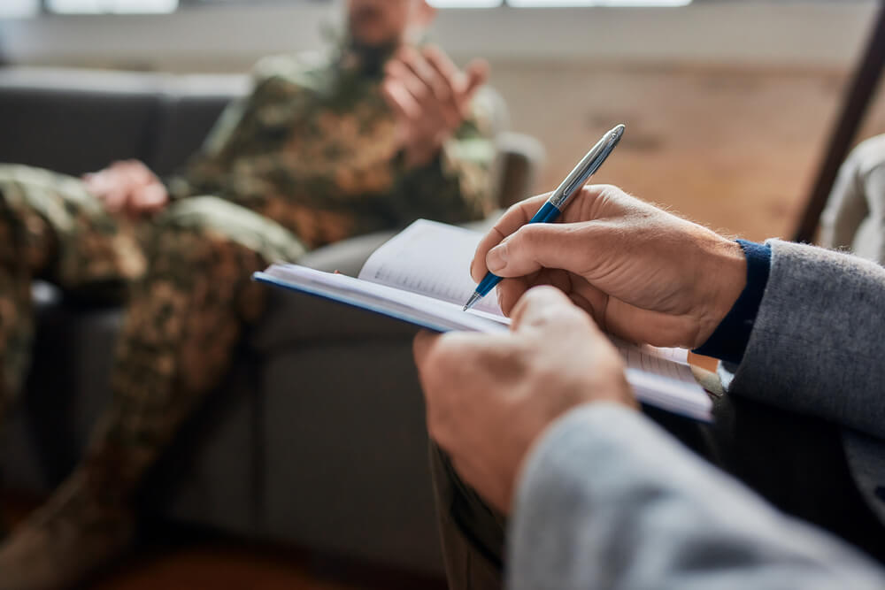 psychologist making notes communicating with military man with PTSD